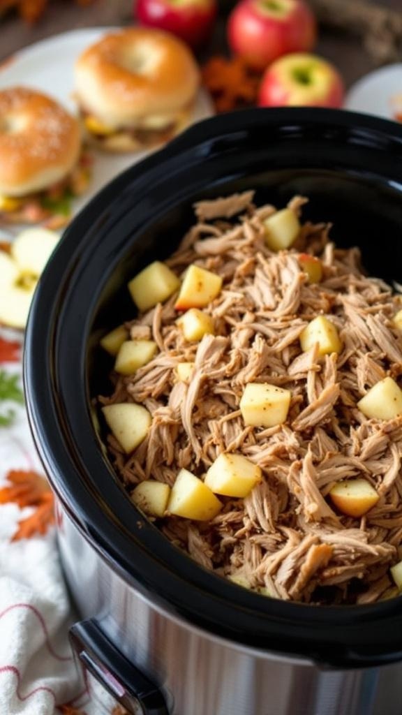 Crockpot filled with apple cider pulled pork and diced apples, with hamburger buns in the background.